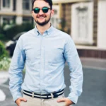handsome-young-businessman-sunglasses-walking-street-he-holds-hands-pockets